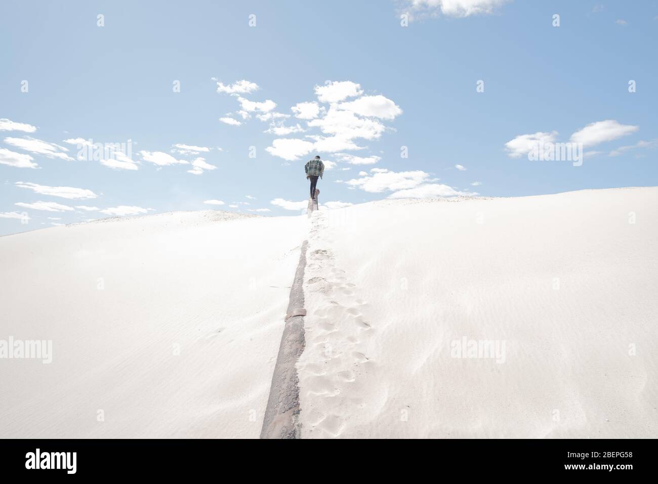 Mann geht weg und hinauf, sandiger Hintergrund. Konzeptuelles Bild Panoramabild in Sand mit Figur der männlichen Person in der Mitte Stockfoto