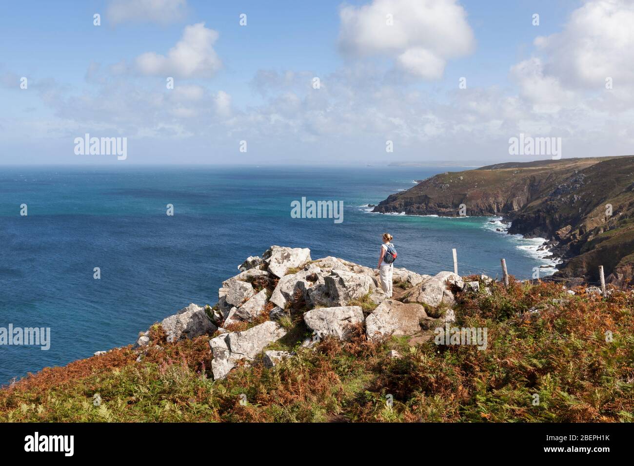 Frau auf einem felsigen Felsen stehend, die die atemberaubende Küstenlandschaft nahe St Ives in Cornwall, England, Großbritannien, betrachtet Stockfoto