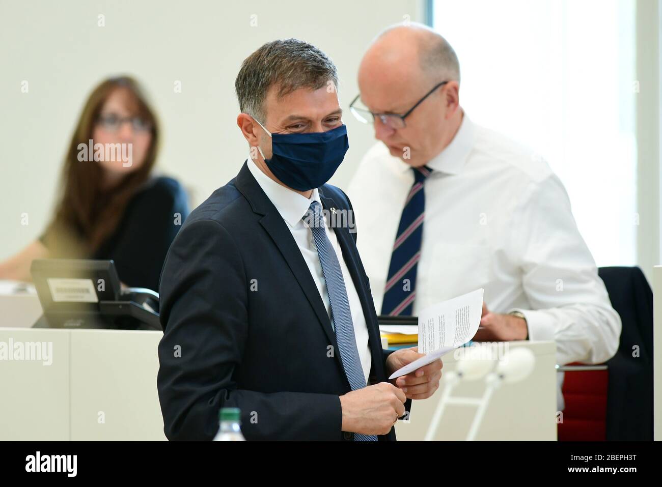 15. April 2020, Brandenburg, Potsdam: Andre Schaller (M, CDU) geht mit einer Gesichtsmaske während der Sondersitzung des Landtags zum Rednerpult. Im Hintergrund sitzen Katrin lange (SPD), die Brandenburger Finanz- und Europaministerin, und Dietmar Woidke (SPD), Ministerpräsident von Brandenburg. Auf der Tagesordnung steht unter anderem ein Gesetzesentwurf von SPD, CDU und Bündnis 90/die Grünen, der die Handlungsfähigkeit der brandenburgischen Kommunen in Ausnahmefällen sicherstellen soll. Foto: Soeren Stache/dpa-Zentralbild/ZB Stockfoto