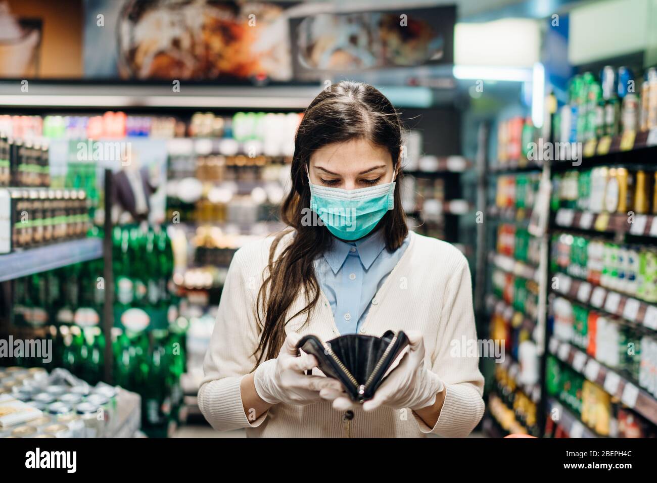 Besorgte Frau mit Maske Lebensmittel einkaufen im Supermarkt Blick auf leere Brieftasche.nicht genug Geld, um Lebensmittel zu kaufen.Covid-19 Quarantäne sperren.Financial Stockfoto