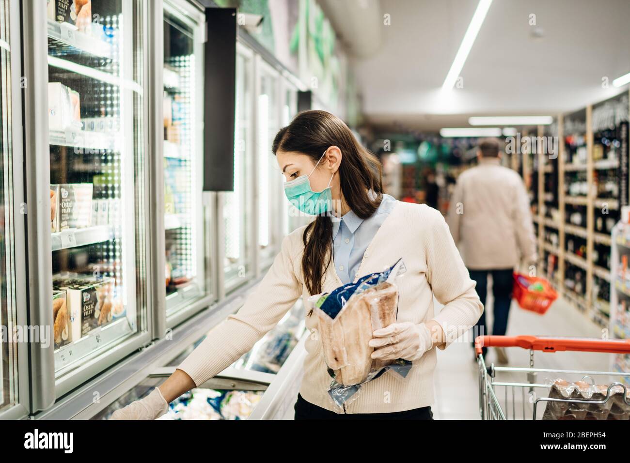 Frau, die Gesichtsmaske trägt, die im Supermarkt kauft.Panic Shopping während Coronavirus Covid-19 Pandemie.Budget Kauf in einem Liefergeschäft.Kauf von Gefriergeräten Smart Stockfoto