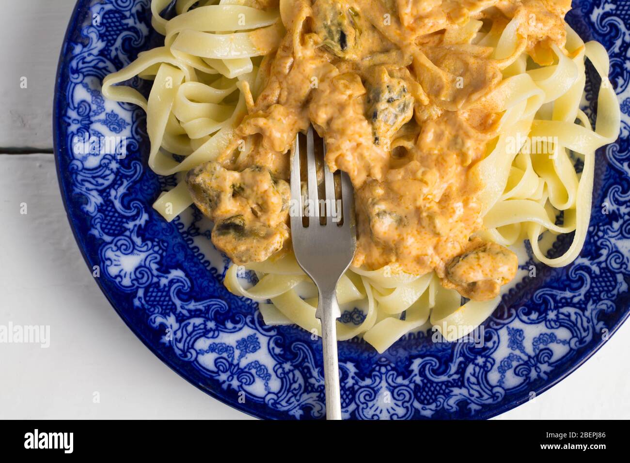 Fettucine Pasta Gericht mit cremigen Muscheln und Käsesauce in blau und weiß Platte - Nahaufnahme von oben Bild Stockfoto