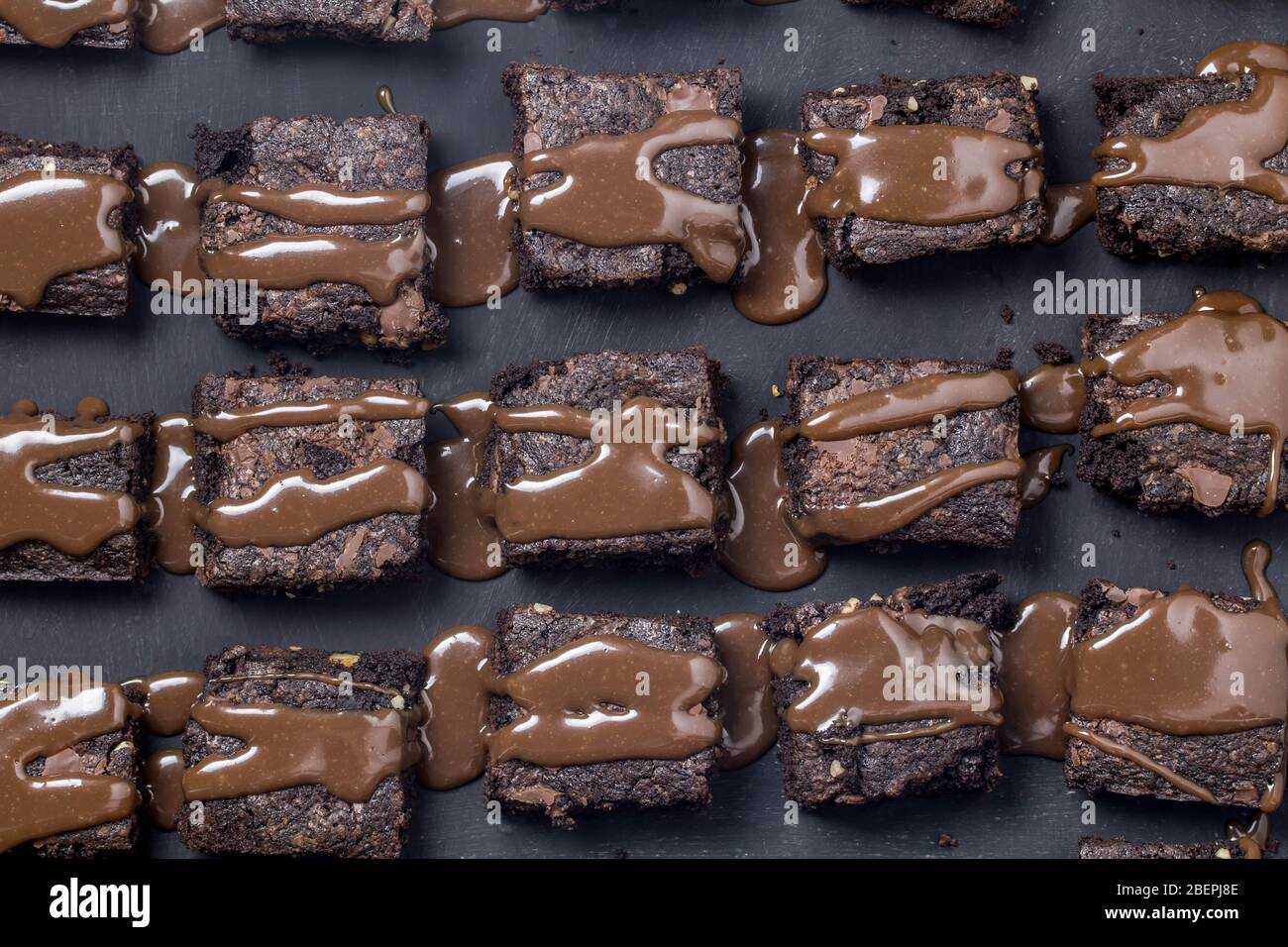Schokoladenkuchen Brownie Quadrate mit Schokolade Ganache Sauce auf schwarzem Hintergrund isoliert tropften Stockfoto