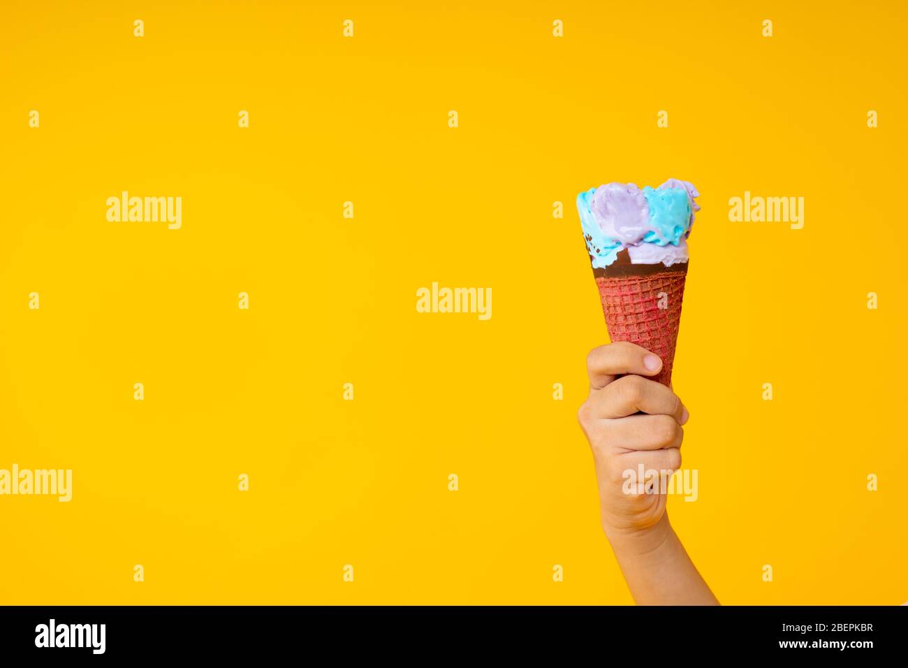 Nahaufnahme Hand hält bunte Eis-Kegel auf gelbem Hintergrund mit Kopierraum Stockfoto