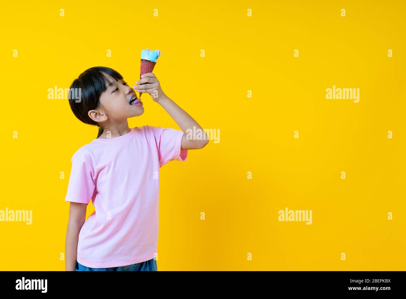 Porträt von jungen asiatischen Mädchen Eis essen, Thai hübsche Kind lecken unten von Kegel auf gelbem Hintergrund Stockfoto