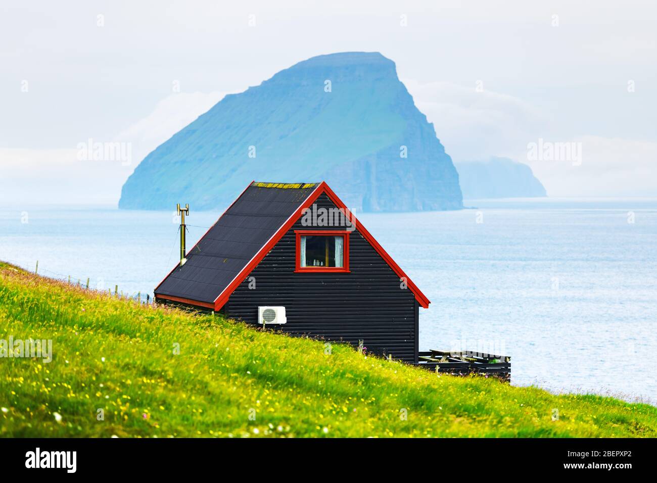 Schwarzes Haus auf dem berühmten färöischen Hexen Finger Trail und der Koltur Insel im Hintergrund. Dorf Sandavagur, Insel Vagar, Inseln der Färöer, Dänemark. Landschaftsfotografie Stockfoto