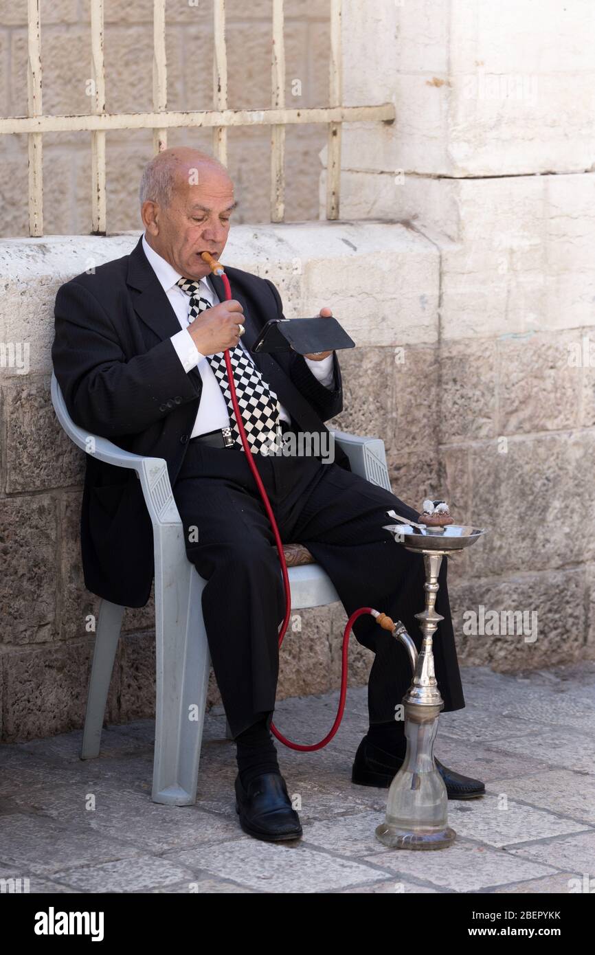 Ein Einheimischer, der einen Anzug trägt und auf der Straße in Jerusalem, Israel, eine Shisha-Pfeife raucht Stockfoto