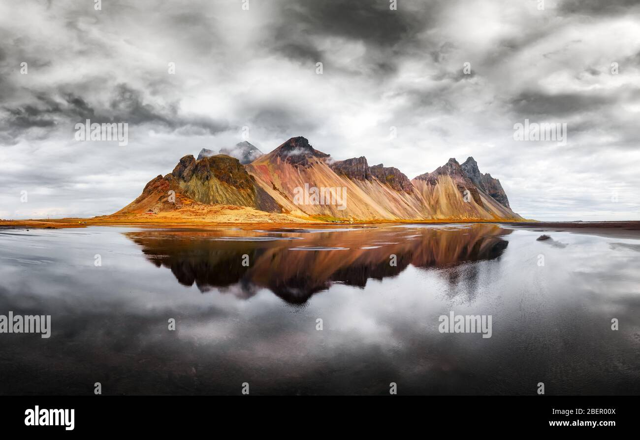 Unglaubliche Landschaft der berühmten Stokksnes Berge auf Vestrahorn Kap. Reflektion im klaren Wasser auf dem epischen Himmel Hintergrund, Island Stockfoto