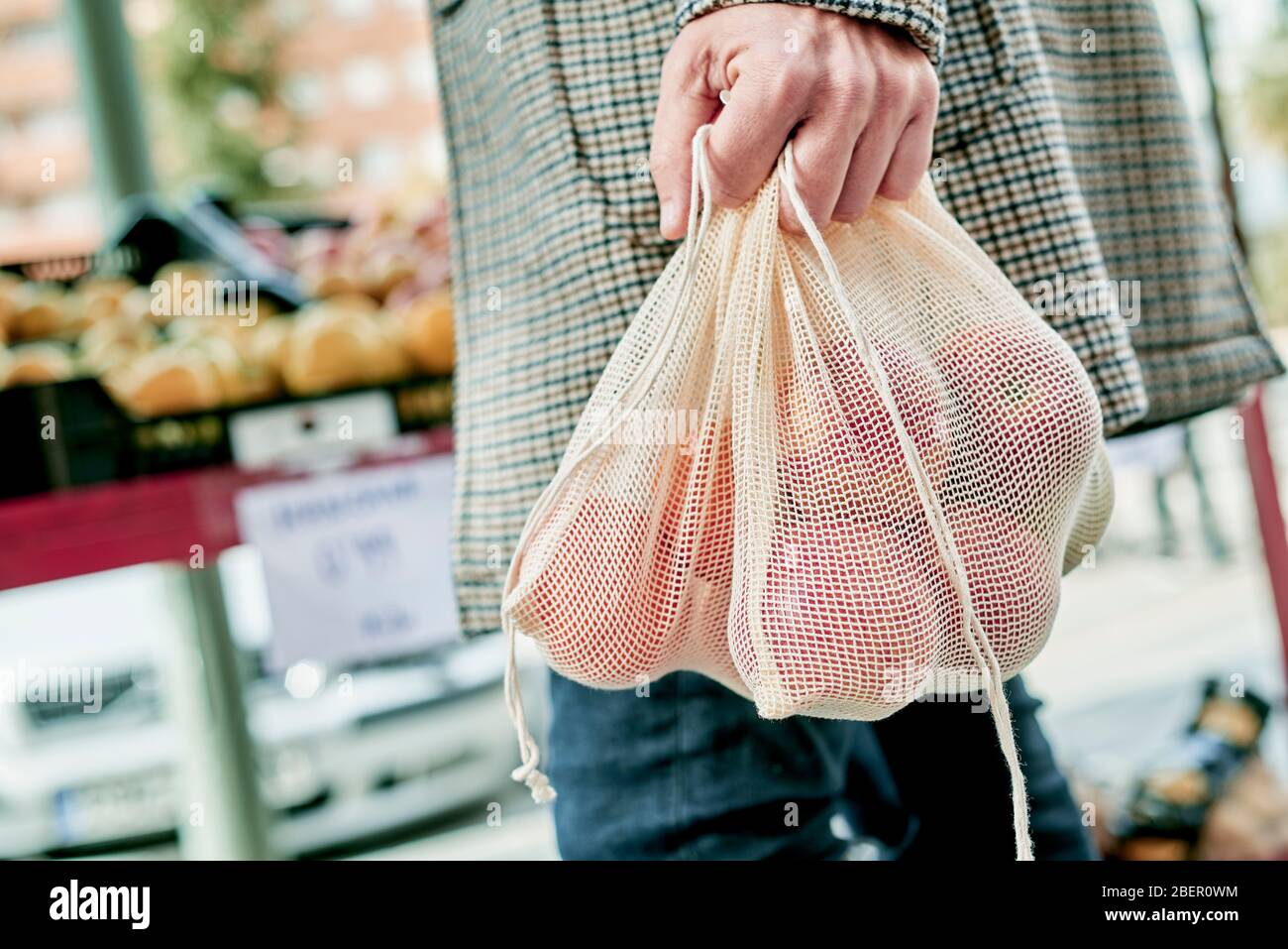 Nahaufnahme eines Mannes, Einkaufen in einem Gemüsehändler oder einem Straßenmarkt, mit einigen textilen wiederverwendbaren Netztüten voller Obst und Gemüse, als Maßnahme zu rot Stockfoto