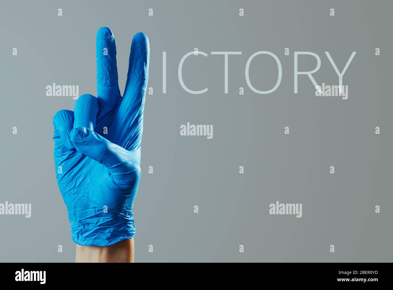 Nahaufnahme der Hand eines Mannes, mit blauen OP-Handschuhe, das V-Zeichen und den Rest der Buchstaben, um das Wort Sieg gegen eine graue Rückseite zu bilden Stockfoto