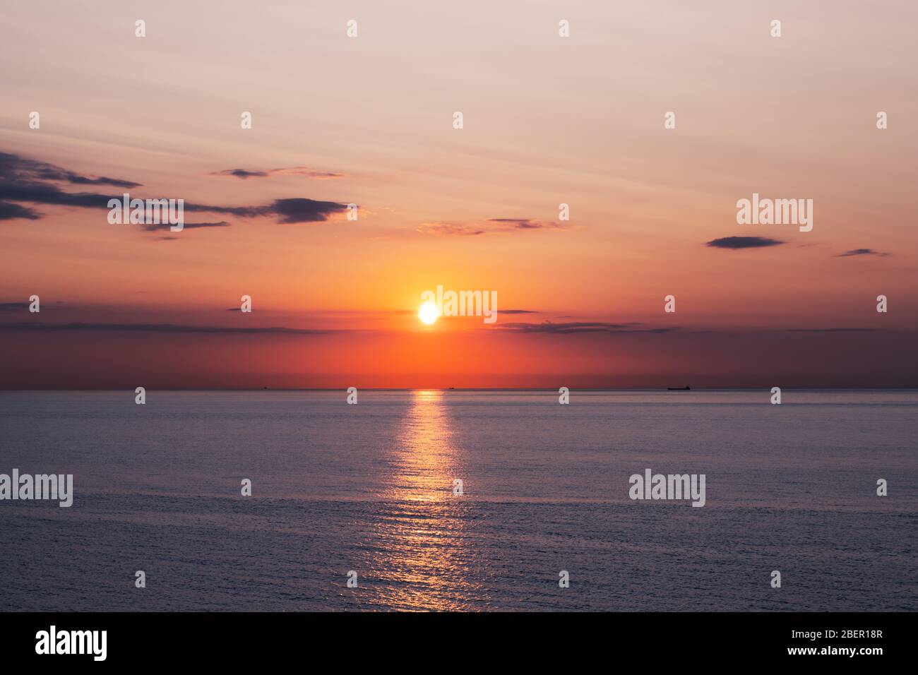 Sonnenuntergang im Meer mit sanften Wellen und rot bewölktem Himmel. Hintergrund des Sonnenaufgangs. Landschaftsfotografie Stockfoto