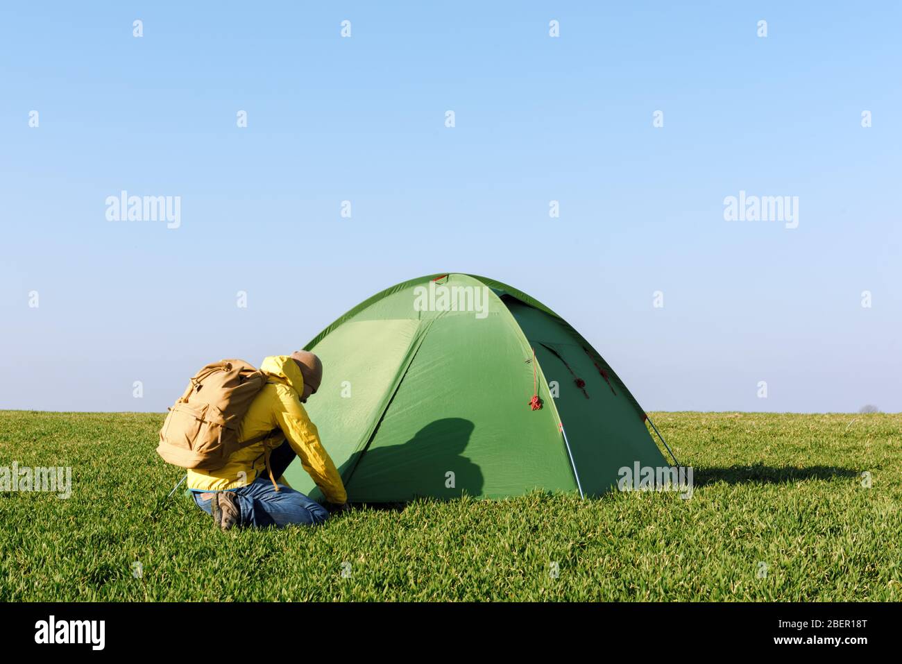 Tourist in gelben Jacke mit Rucksack in der Nähe seines Zeltes auf Sommerfeld. Blauer Himmel. Reise- und Abenteuerkonzept Stockfoto