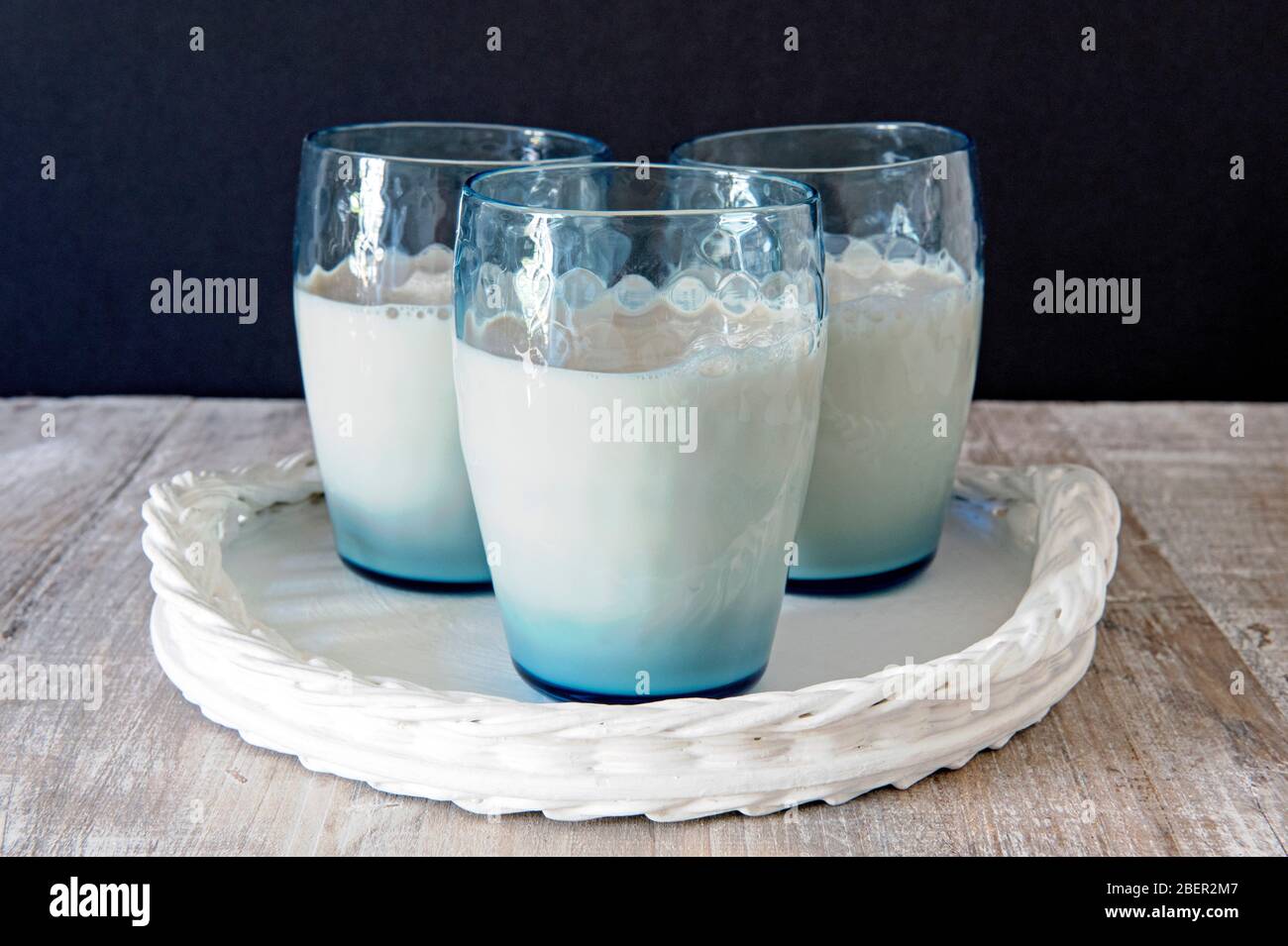 Drei blaue Vintage-Gläser oder Becher veganer Hafermilch auf weißem Tablett mit schwarzem Hintergrund Stockfoto