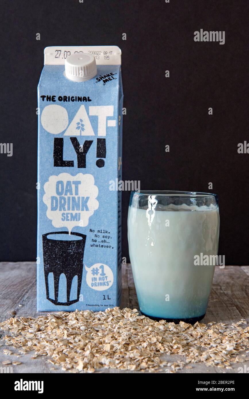Vegan Oatly Milk Drink in blauem Vintage Glas mit dem Original Oatly Hafertrunk Karton hinten und Hafer mit schwarzem Hintergrund. Editorale Verwendung Stockfoto
