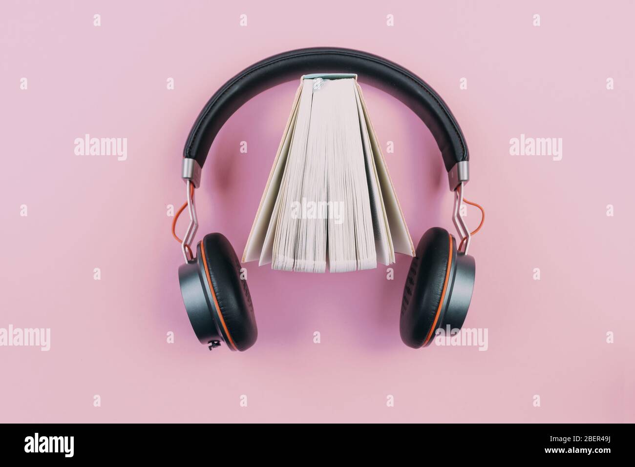 Hörbuch-Konzept, Ansicht von Stereokopfhörern und ausgefächeltes Hardcover-Buch auf rosa Desktop Stockfoto