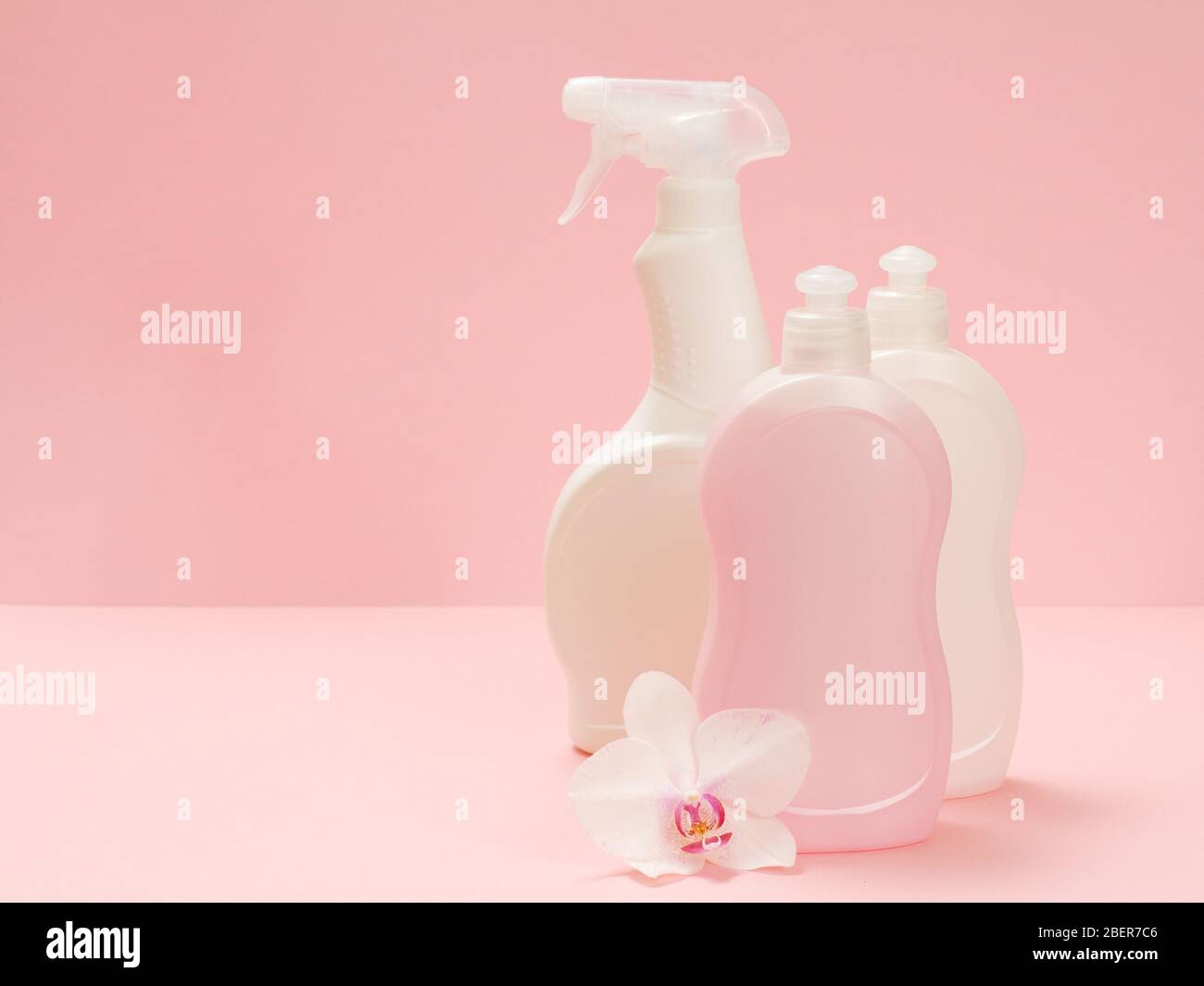 Plastikflaschen mit Spülmittel, Glas- und Fliesenreiniger, Spülmittel für Mikrowellenherde und Herde und eine weiße Orchideenblume auf rosa Hintergrund Stockfoto