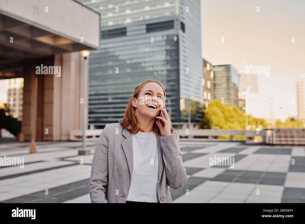 Glückliche junge Geschäftsfrau in formeller Kleidung im Gespräch über Smartphone Stockfoto