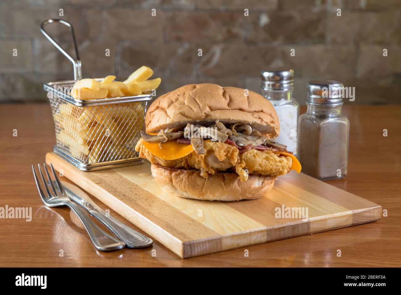 Burger mit Schnitzel, pommes Frites und Champignons. Sandwich mit gebratenem Fleisch, Speck, Käsepilzen und Sieb mit Chips auf Holzplatte neben c Stockfoto