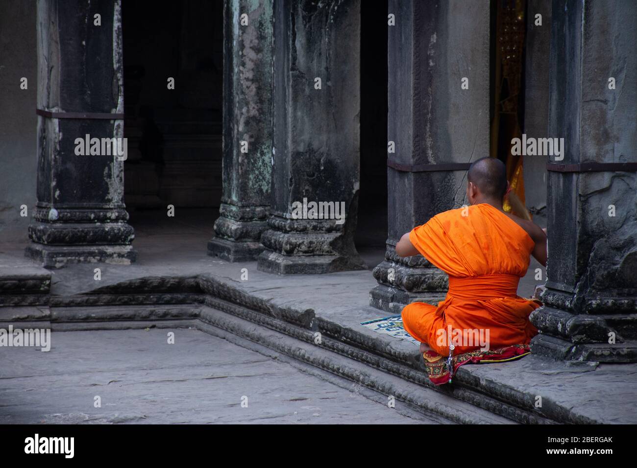 Ein einiger Mönch in leuchtend orangen Gewändern betet an einem alten Tempel, Angkor Wat, Kambodscha. Stockfoto