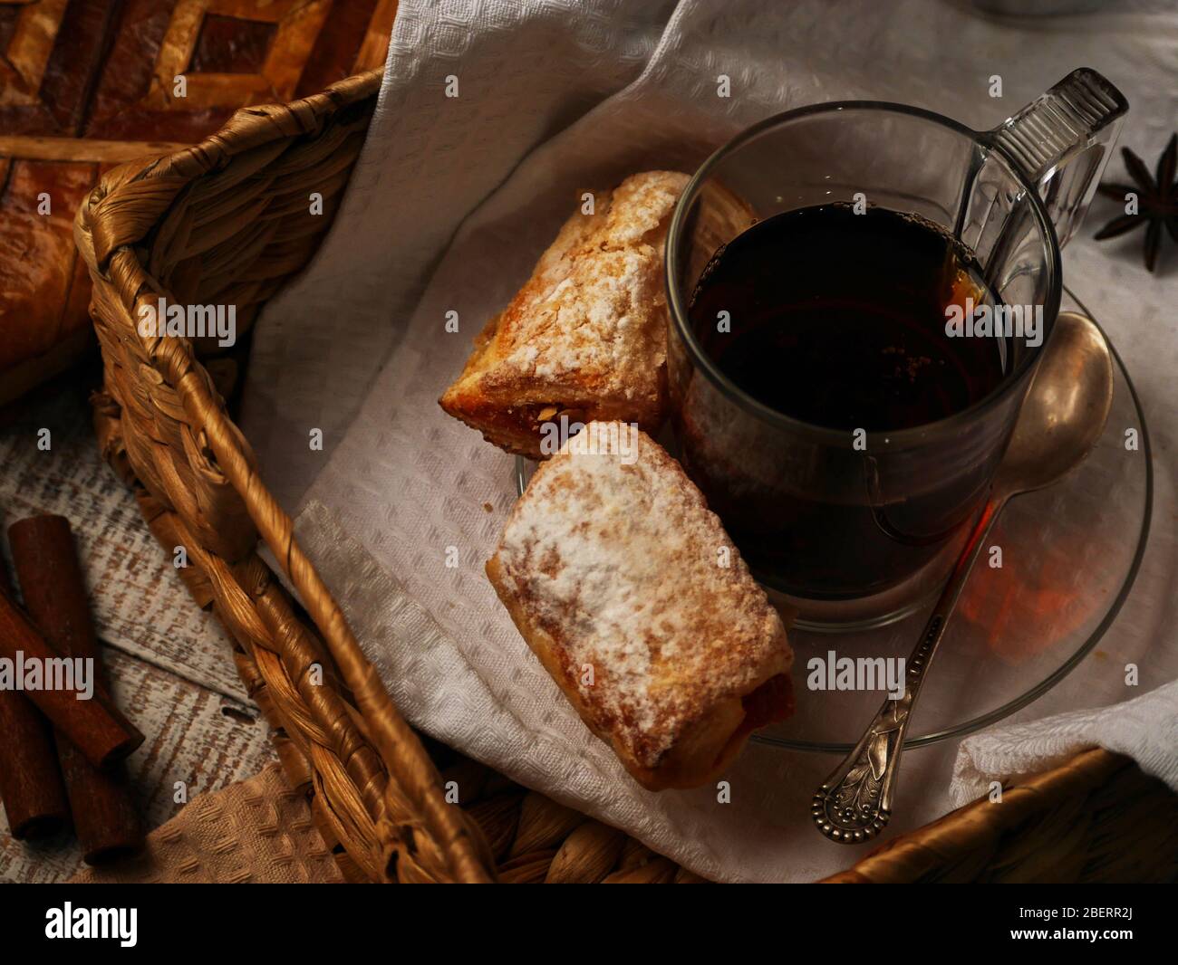 Tee mit süßen Plätzchen in einem Weidenkorb auf weißem Holzhintergrund. Zimtstiele lagen in der Nähe des Nachmittags-Tees Stockfoto