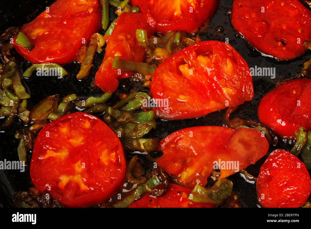 In Scheiben geschnittene Tomaten und Paprika werden in einer Pfanne gebraten Stockfoto