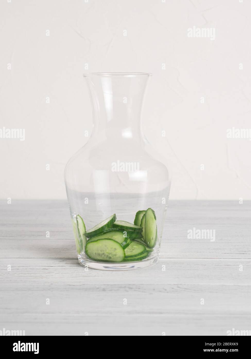 Glas mit Gurkenscheiben innen für Gurkenwasser Rezept. Flasche mit Gurke auf weißem Tisch. Schritt, um Detox Wasser zu machen Stockfoto
