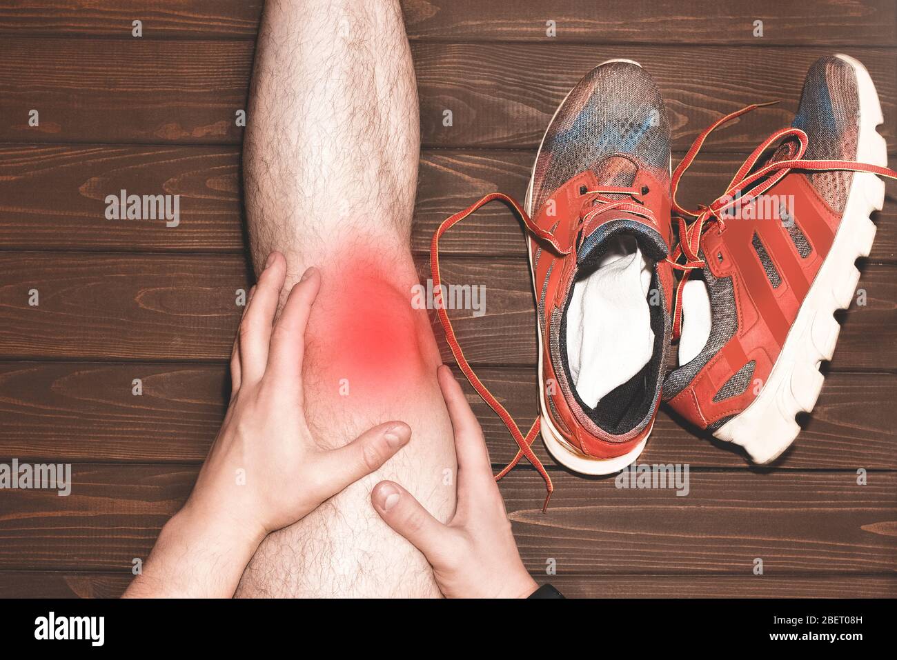 Junger Sportmann mit starken athletischen Beinen, der das Knie mit seinen Händen in Schmerzen hält, nachdem er während eines Lauftrainings auf woo eine Bandverletzung erlitten hat Stockfoto