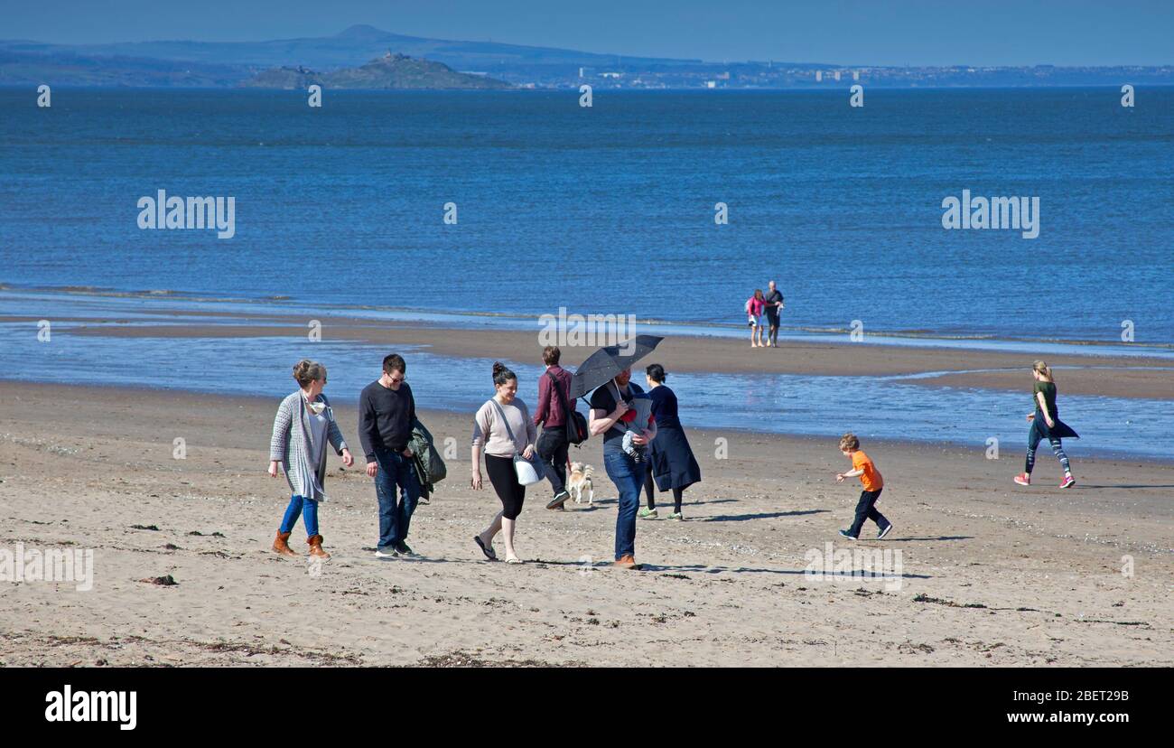 UK Wetter: Sonnenschein an einem sehr ruhigen Portobello Strand. Edinburgh, Schottland, Großbritannien. April 2020. Temperatur von 17 Grad aber eine leichte kühle Brise am Meer, hält diese Familie ihr Baby unter dem Schatten eines Sonnenschirms, während sie auf dem Sandstrand spazieren. Menschenmassen bleiben weg und beachten die Warnungen, wegen der Coronavirus-Sperre zu Hause zu bleiben. Quelle: Arch White / Alamy Live News. Stockfoto