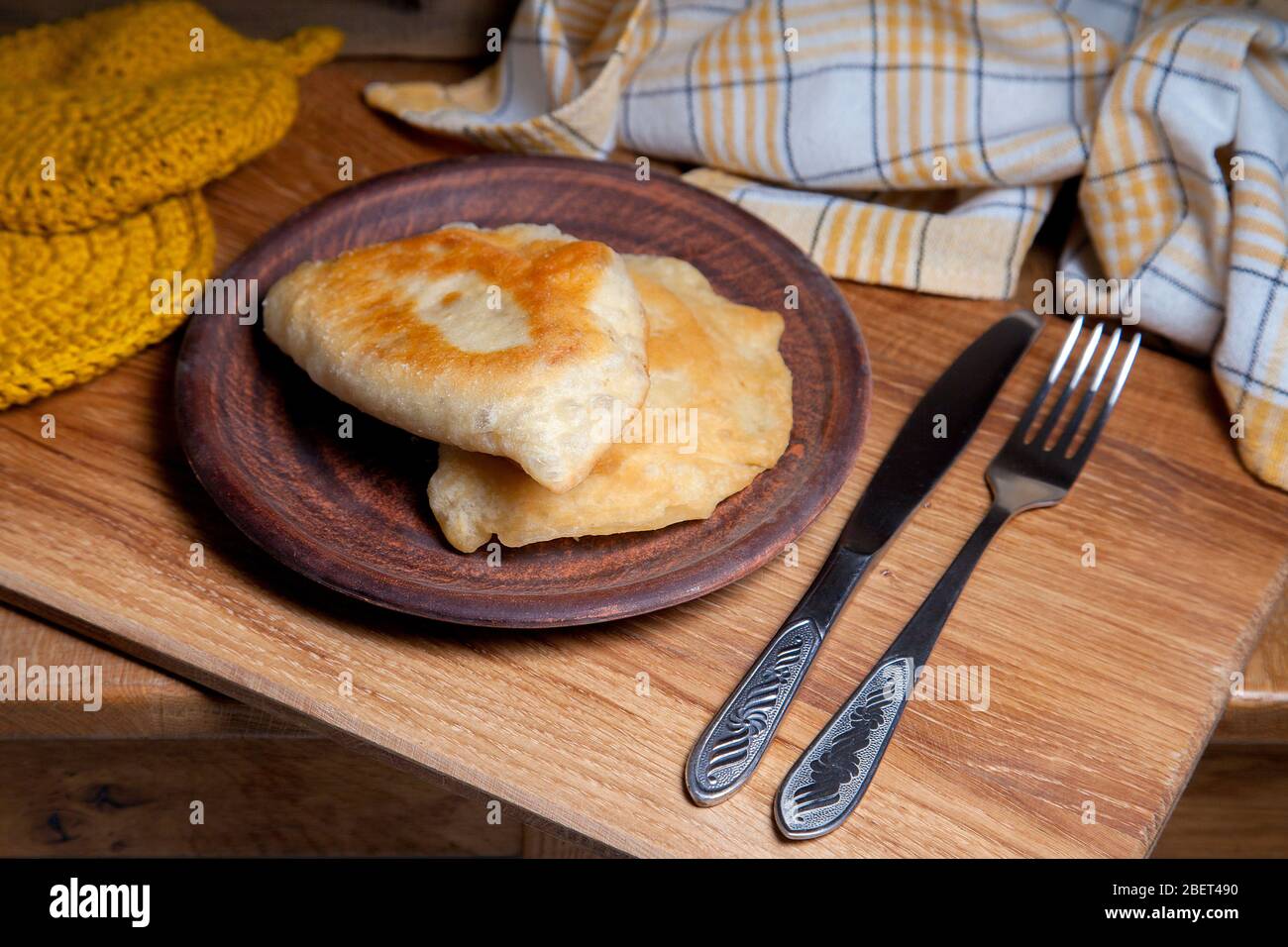 Tonplatte mit zwei einzelnen gebratenen Pasteten mit Fleisch auf Holztisch. Komposition aus Fast-Food-Abendessen und Besteck im rustikalen Stil auf Vintage-Holz Stockfoto