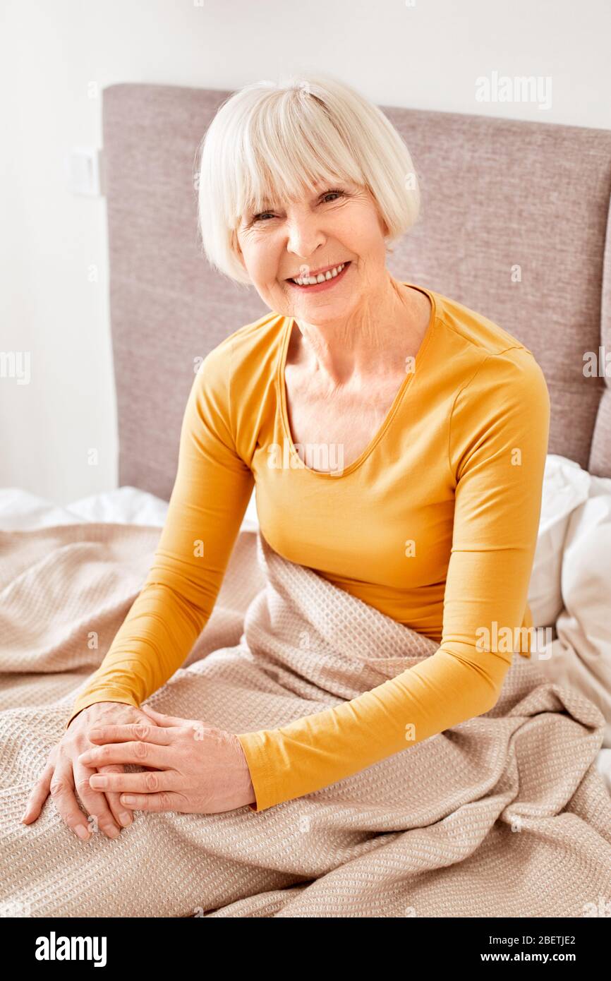 Ruhestand. Ältere Frau, die zu Hause auf dem Bett liegt und fröhlich lächelt Stockfoto