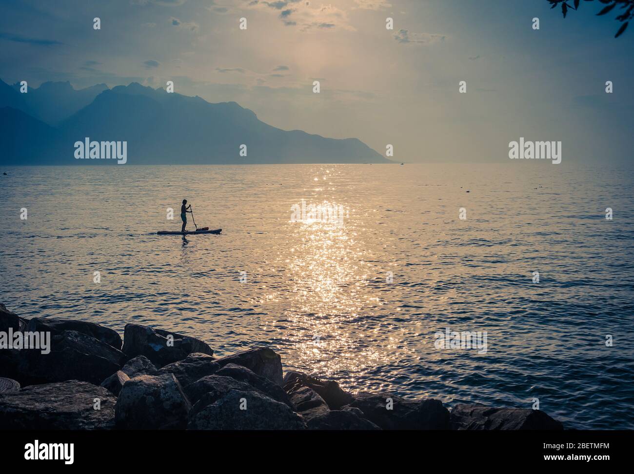Figur Silhouette eines Mannes auf einem Surfbrett mit Paddel auf dem Genfer See in Montreux vor den Bergen Alpen, Schweizer Riviera, Waadtland Cant Stockfoto