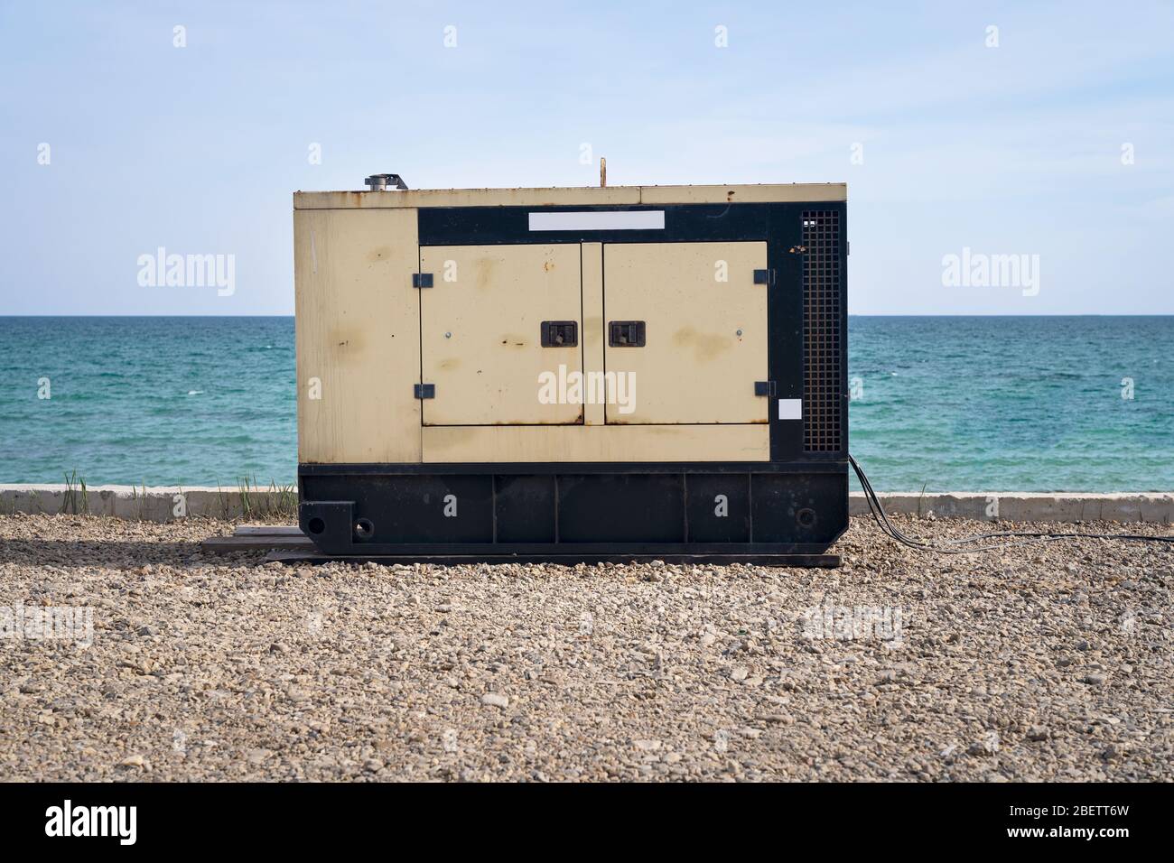 Ein elektrischer Dieselgenerator steht am Strand vor dem Hintergrund des Meeres und des blauen Himmels. Eine unabhängige Energiequelle, die Unterstützung wi Stockfoto