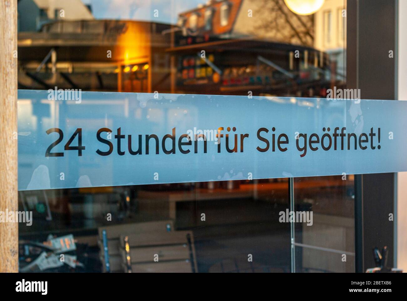 Schaufenster eines Geschäfts mit einem Schild "Open 24 Hours for You", in deutscher Sprache, mit Displays und die Reflexion der Umgebung in Unschärfe zum Zeitpunkt der Stockfoto