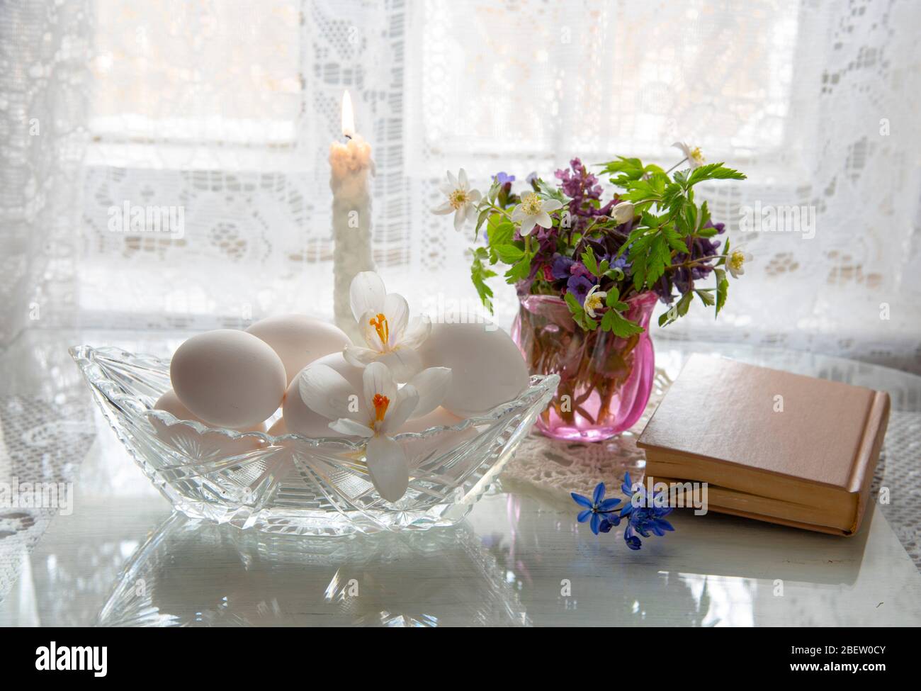Frühlingsblumen in einem Glas und weißen Eiern in einer Kristallvase auf weißem Grund. Stockfoto
