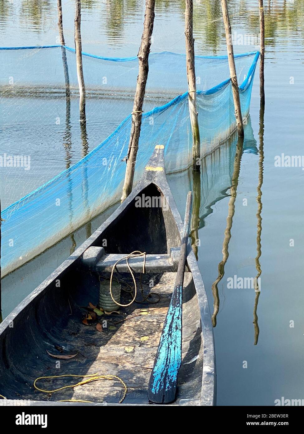 Holzkanu mit blau lackiertem Ruder, angedockt von einer Fischfarm Stockfoto