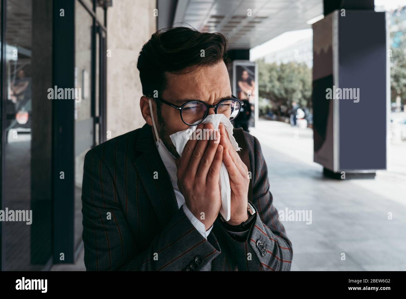 Kranker Mann mit schützender Gesichtsmaske hustet und niest auf der Straße. Stockfoto