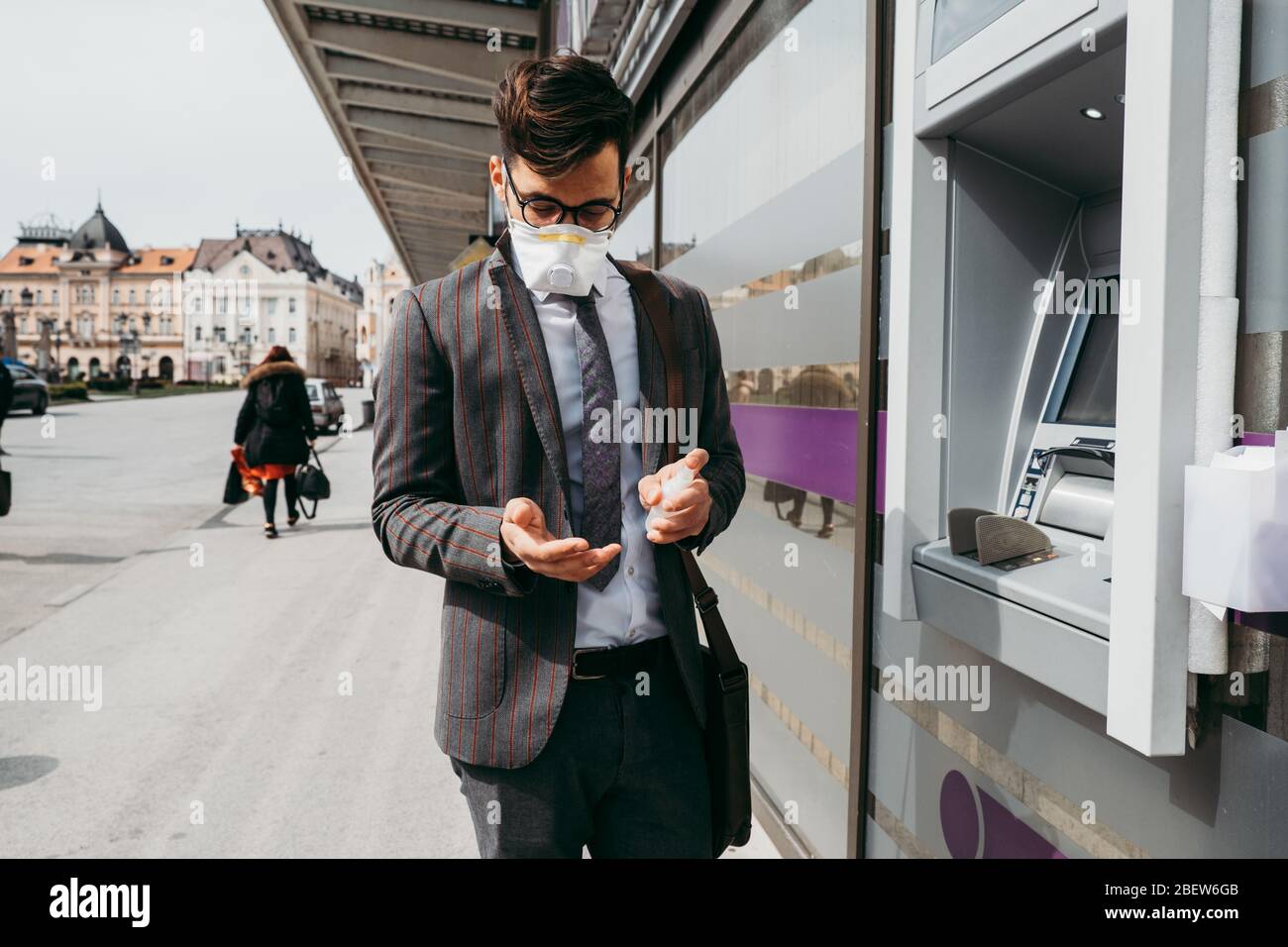 Der Mensch desinfiziert seine Hände nach dem Gebrauch des Geldautomaten mit Alkoholspray Stockfoto