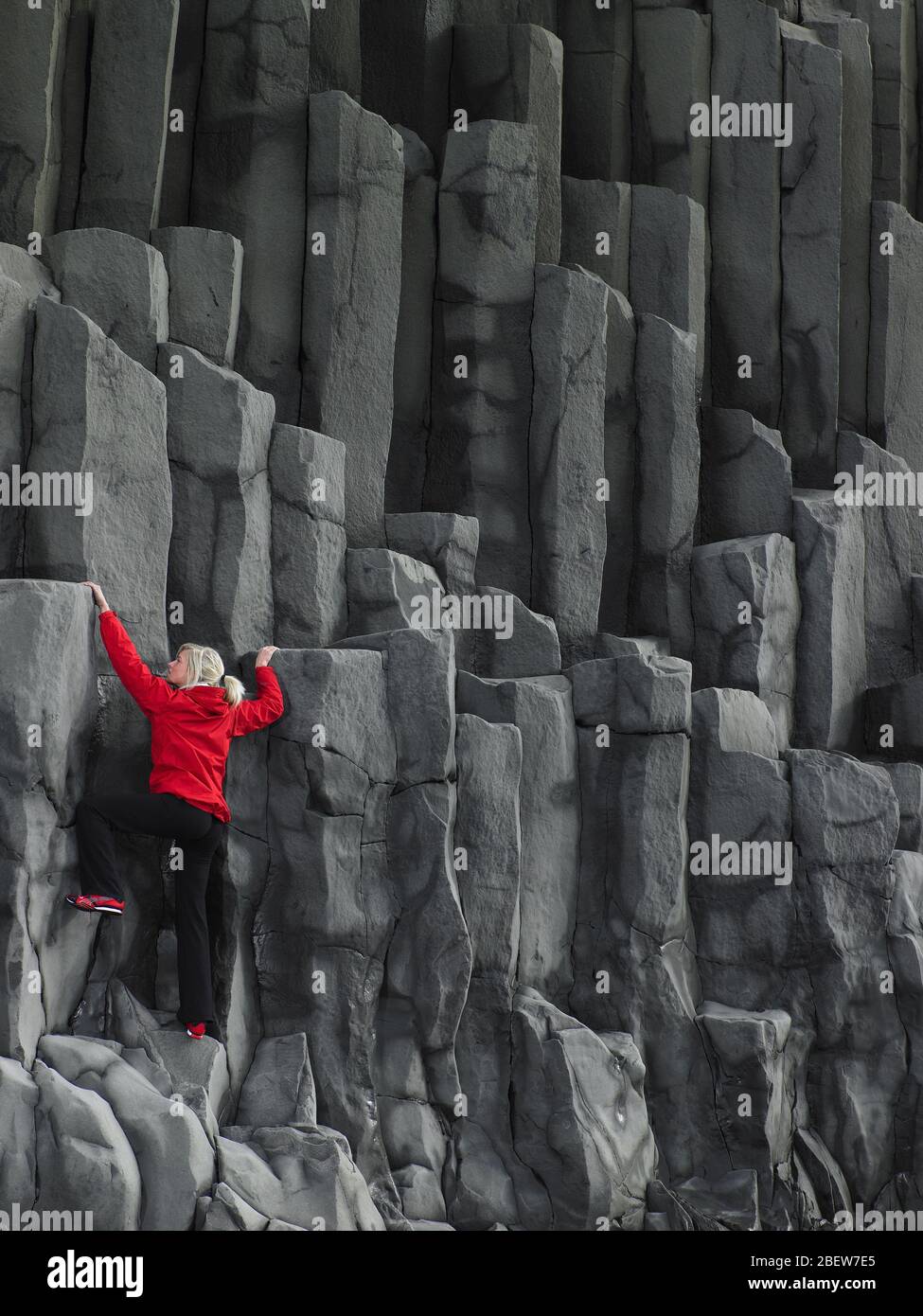 Frau, die Basaltsäulen in Südisland erklimmen Stockfoto
