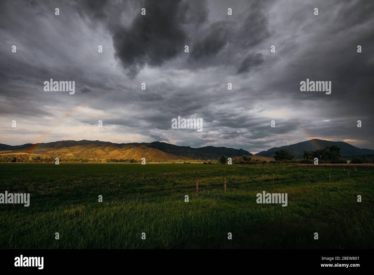 Subtiler Regenbogen in stürmischen Wolken in leerem stimmungsvollem Feld Stockfoto