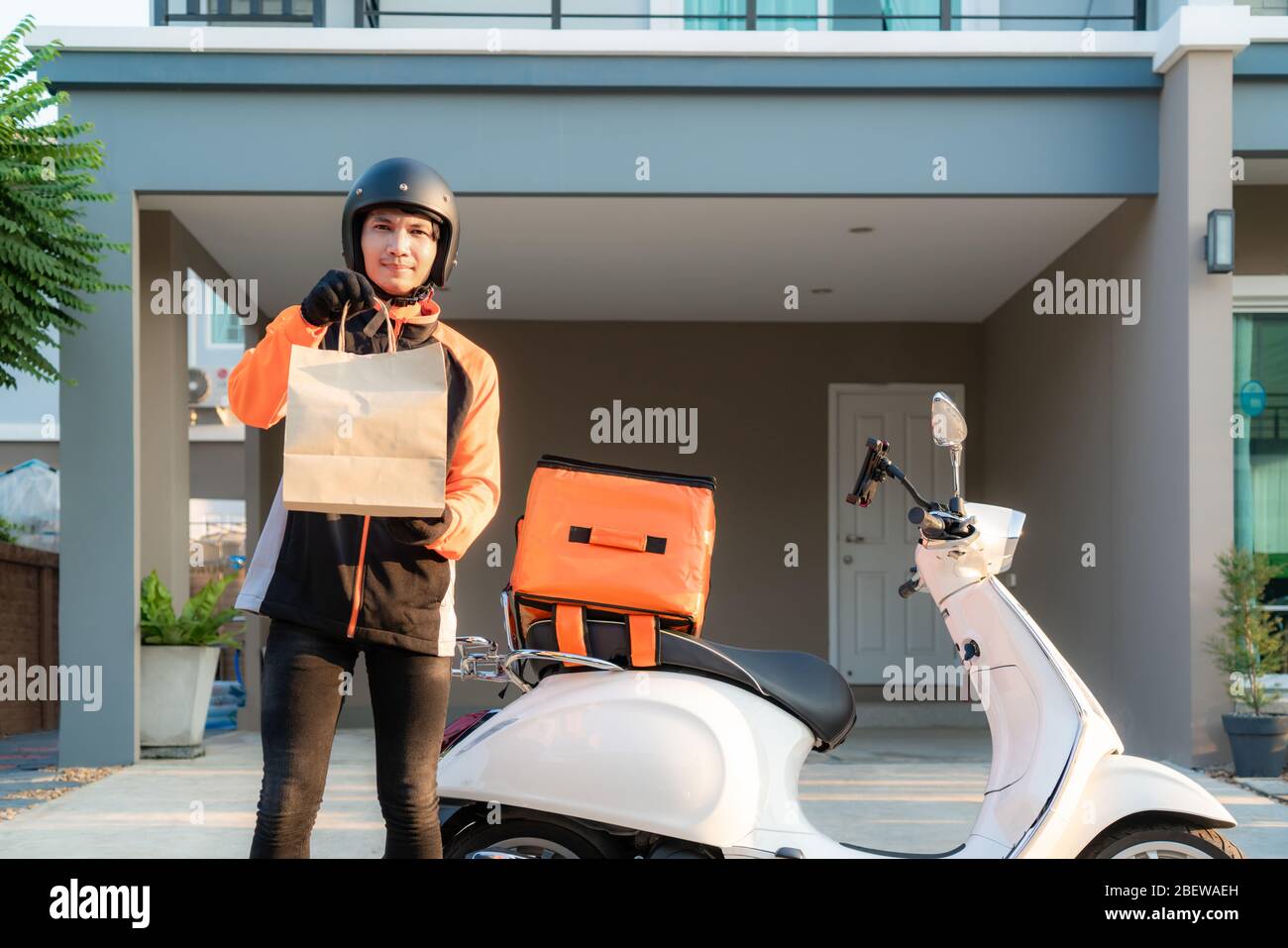 Lieferung Asian Mann trägt orange Uniform und bereit zu senden liefern Lebensmitteltasche vor dem Kunden houes mit Case Box auf Roller, Express-Lebensmittel-Deli Stockfoto