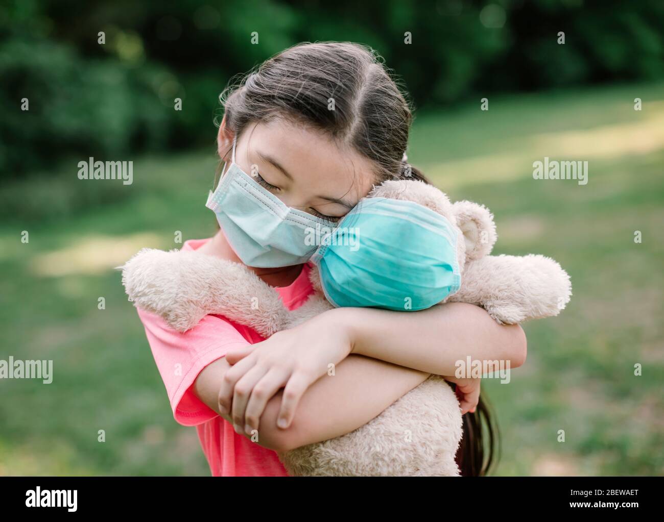 Stress kleines Mädchen hält Spielzeug Bär in medizinischen Schutzmaske Stockfoto