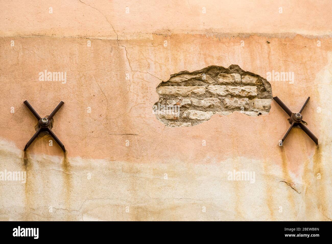 Die abgekratzte Wand des alten Gebäudes mit rostigen Eisenspikes der Balken, um das Haus zu stabilisieren Stockfoto