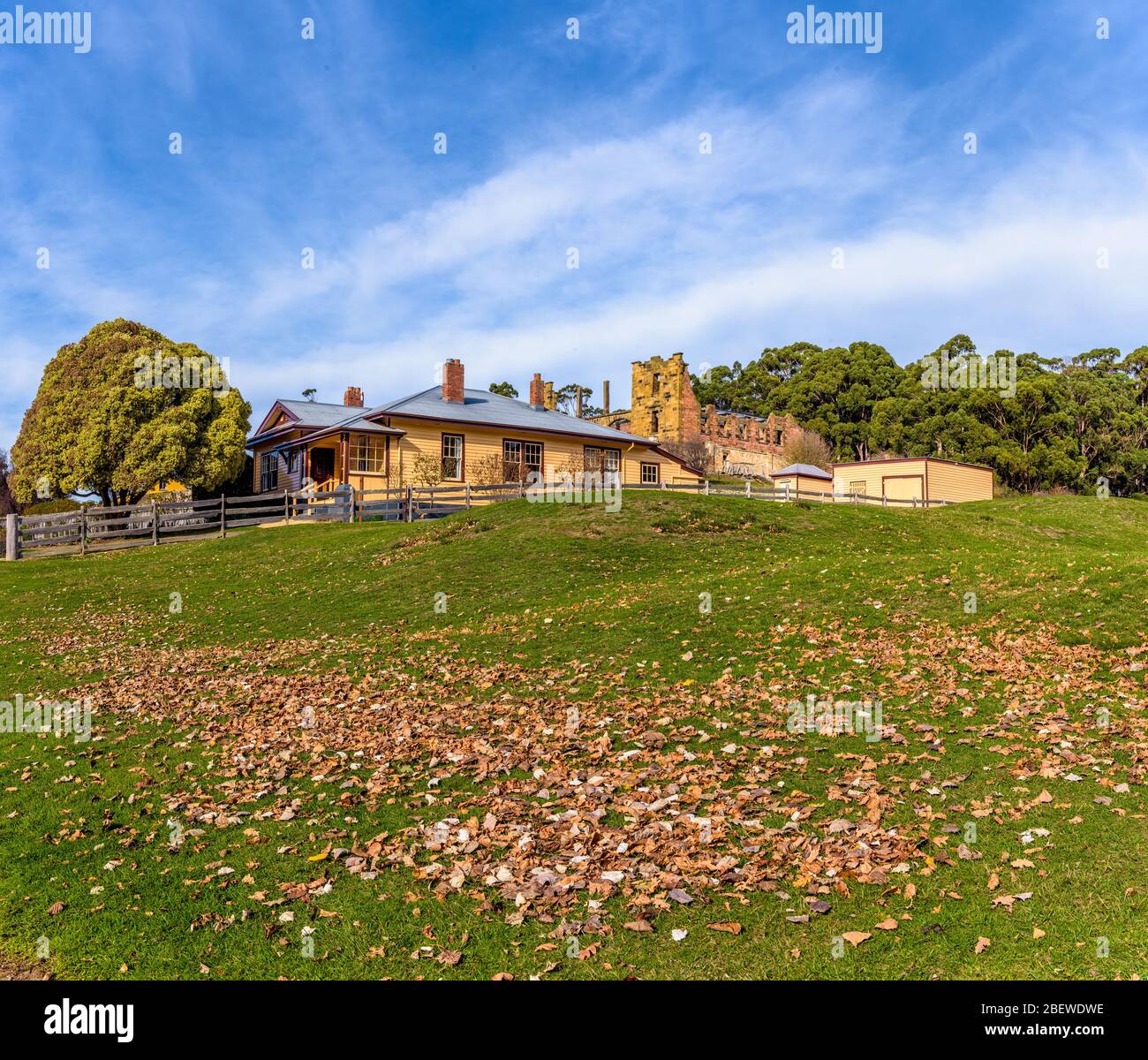 Im Vordergrund grasbewachsenes Fahrerlager mit gefallenen Blättern, das zum Canadian Cottage Port Arthur Historical Site in Tasmania Australien führt. Stockfoto