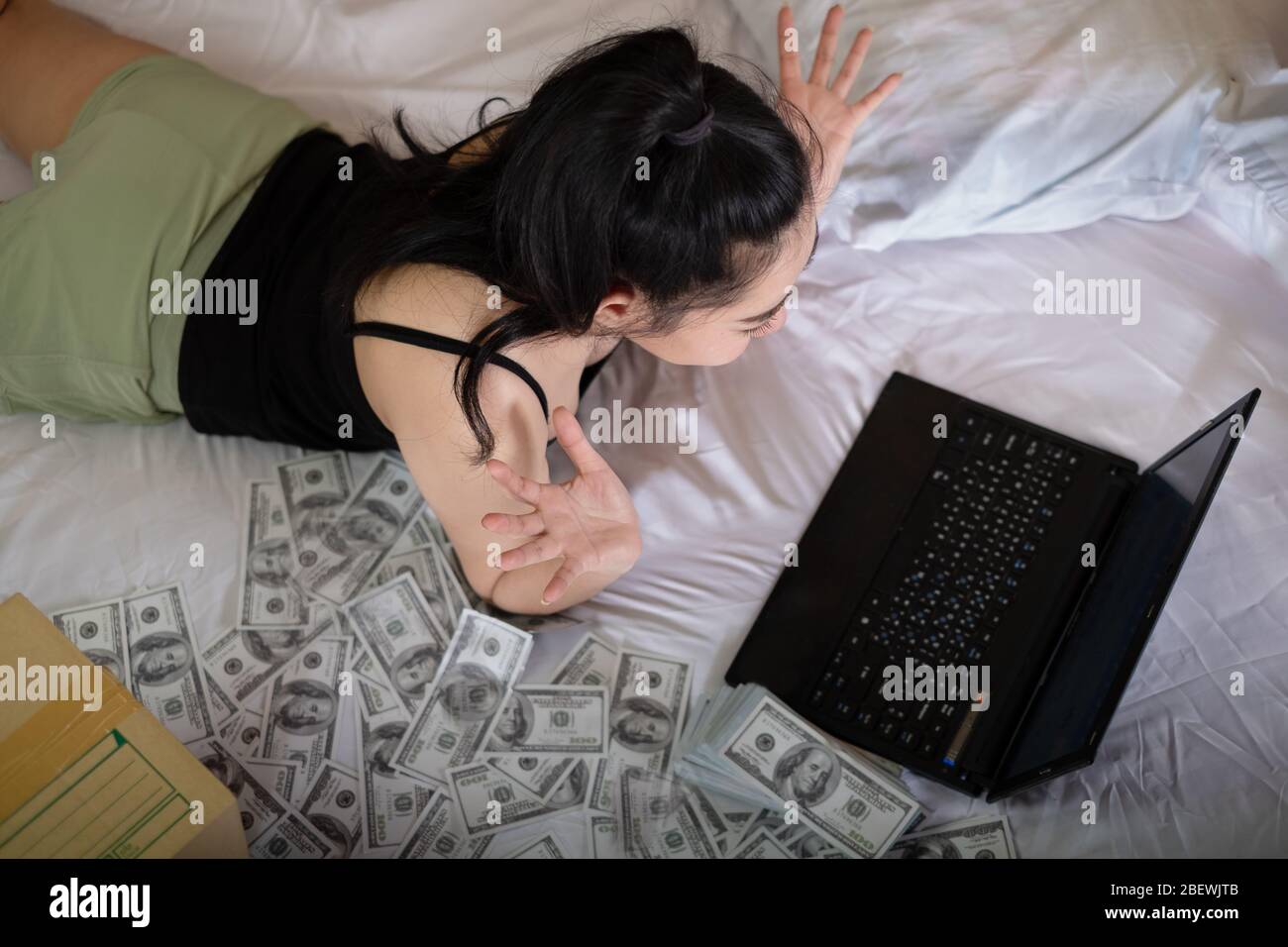 Portrait Attraktive junge Asienfrau legte sich auf das Bett und arbeitete auf einem Laptop im Schlafzimmer mit Stapel 100 US-Dollar Banknoten eine Menge, arbeitet von o Stockfoto