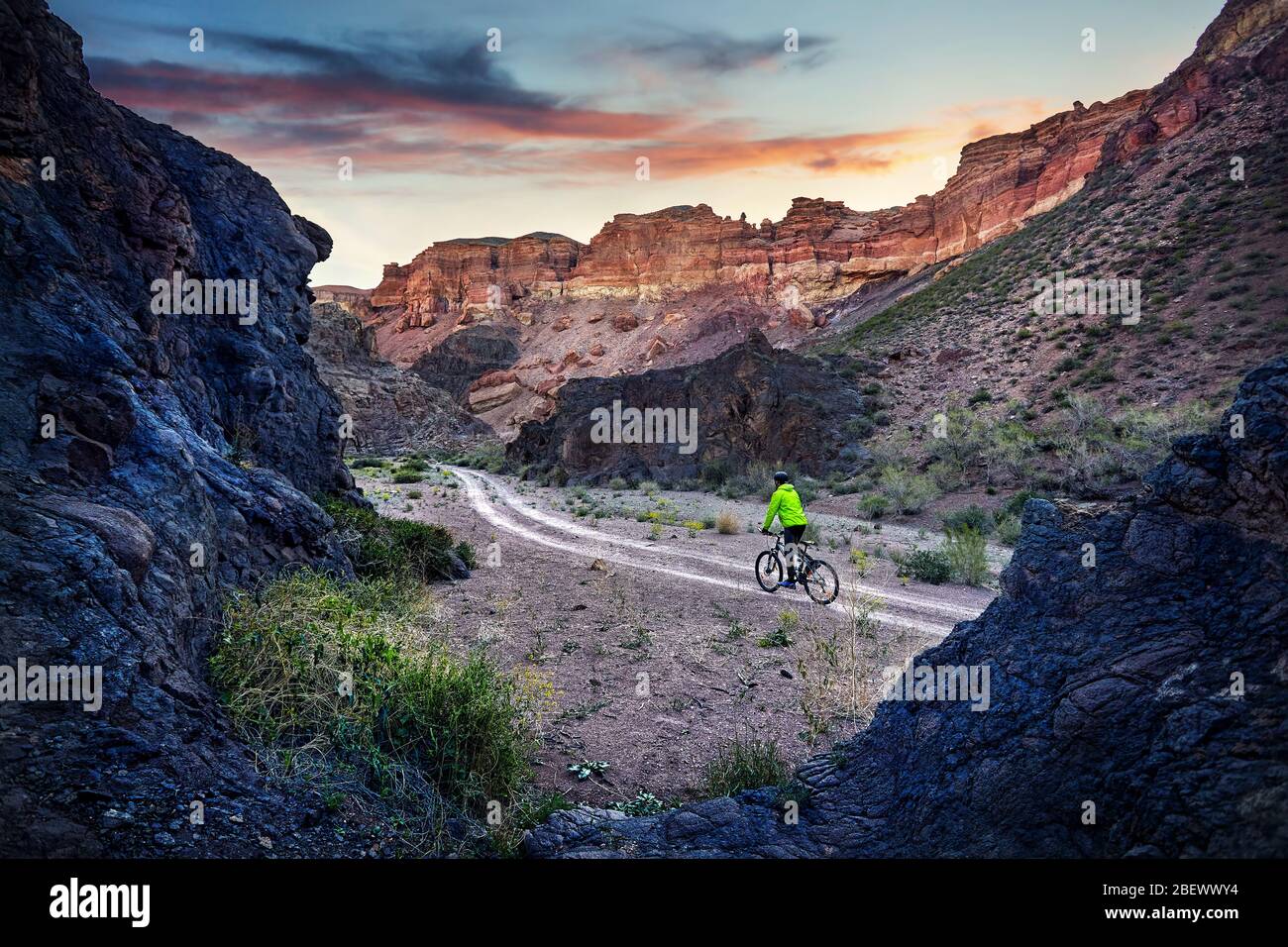Reiter in grüne Jacke an Mountainbike in der Wüste Charyn Canyon bei Sonnenaufgang in Kasachstan. Extreme Sport Konzept. Stockfoto