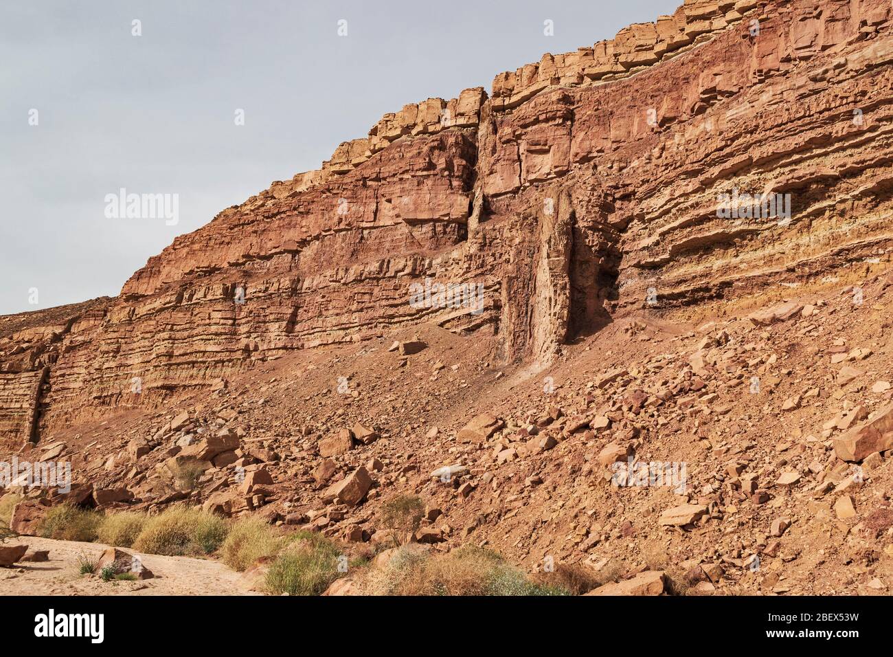 Geologische Details der Klippe neben wadi ardon im Krater makhtesh ramon, die zwei Magmadeiche mit dem Bachbett im Vordergrund zeigt Stockfoto