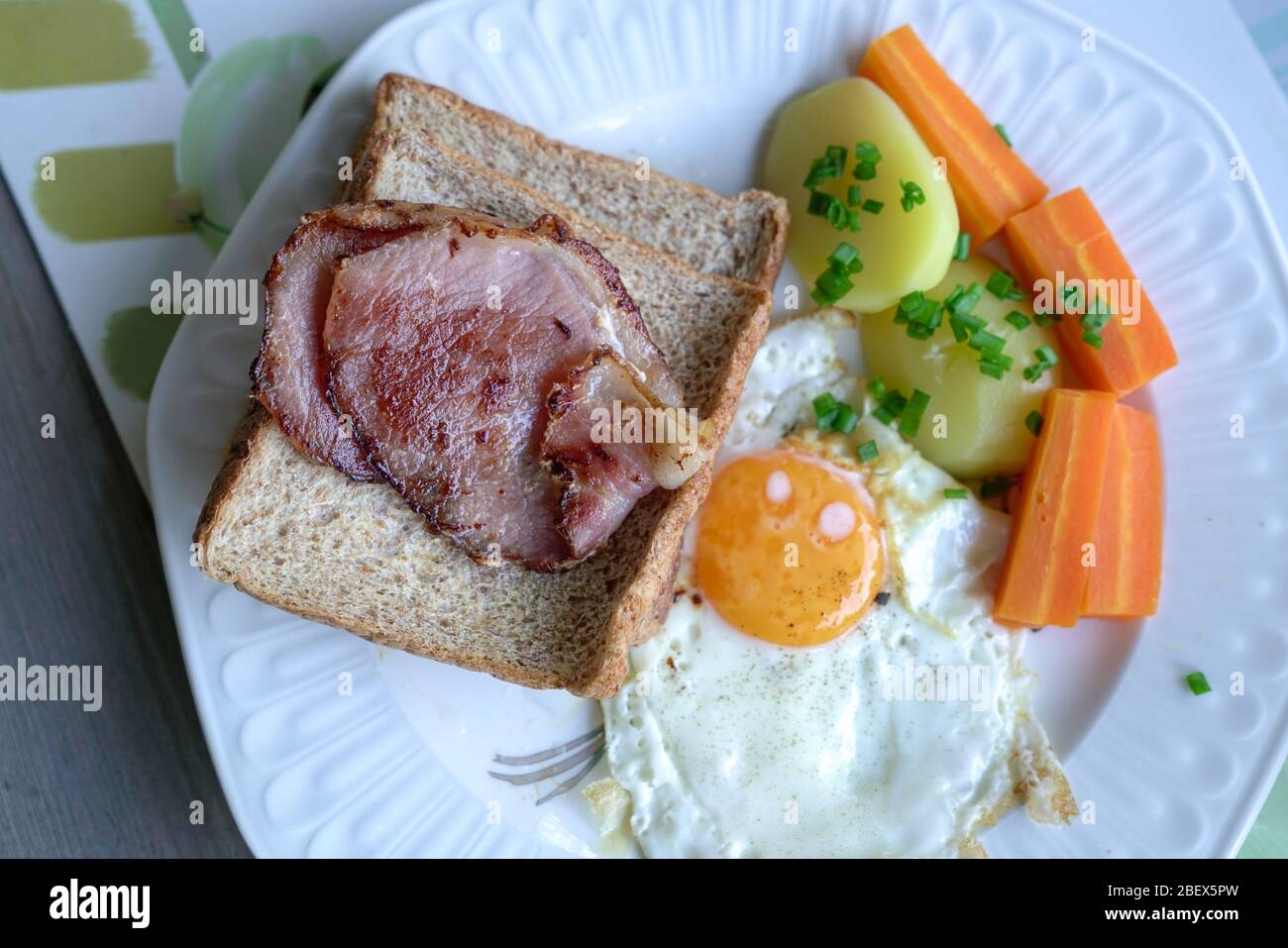 Frühstück mit Speck, Ei, Kartoffeln, Karotten und Brot. Draufsicht. Stockfoto