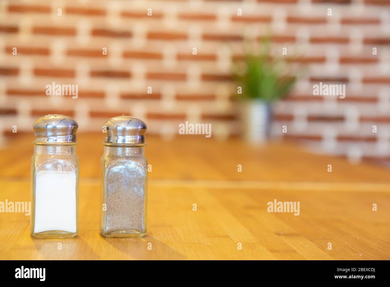 Pfefferstreuer und Salt Shaker auf einem Bambus Tisch mit einem Ziegelstein Hintergrund Stockfoto
