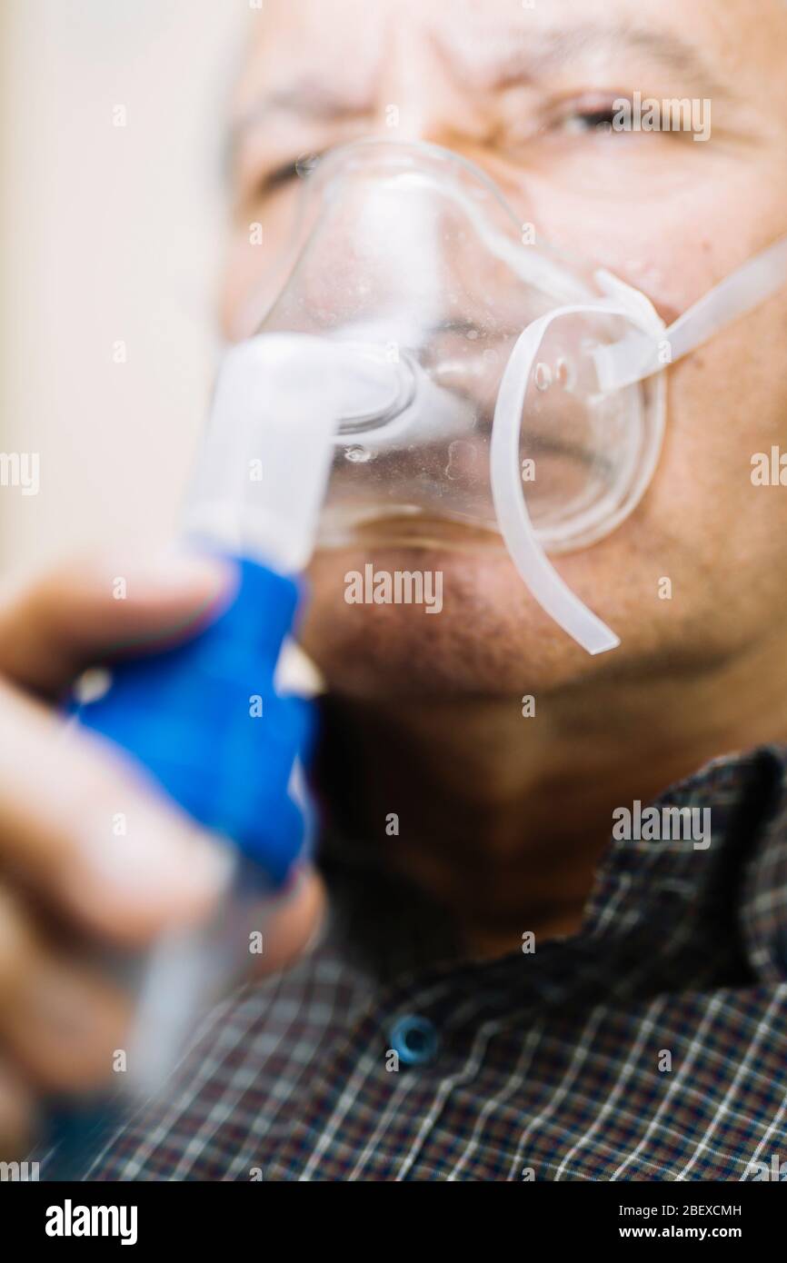 Leitender Mann, der medizinische Geräte für die Inhalation mit Atemschutzmaske verwendet, Vernebler im Zimmer Stockfoto