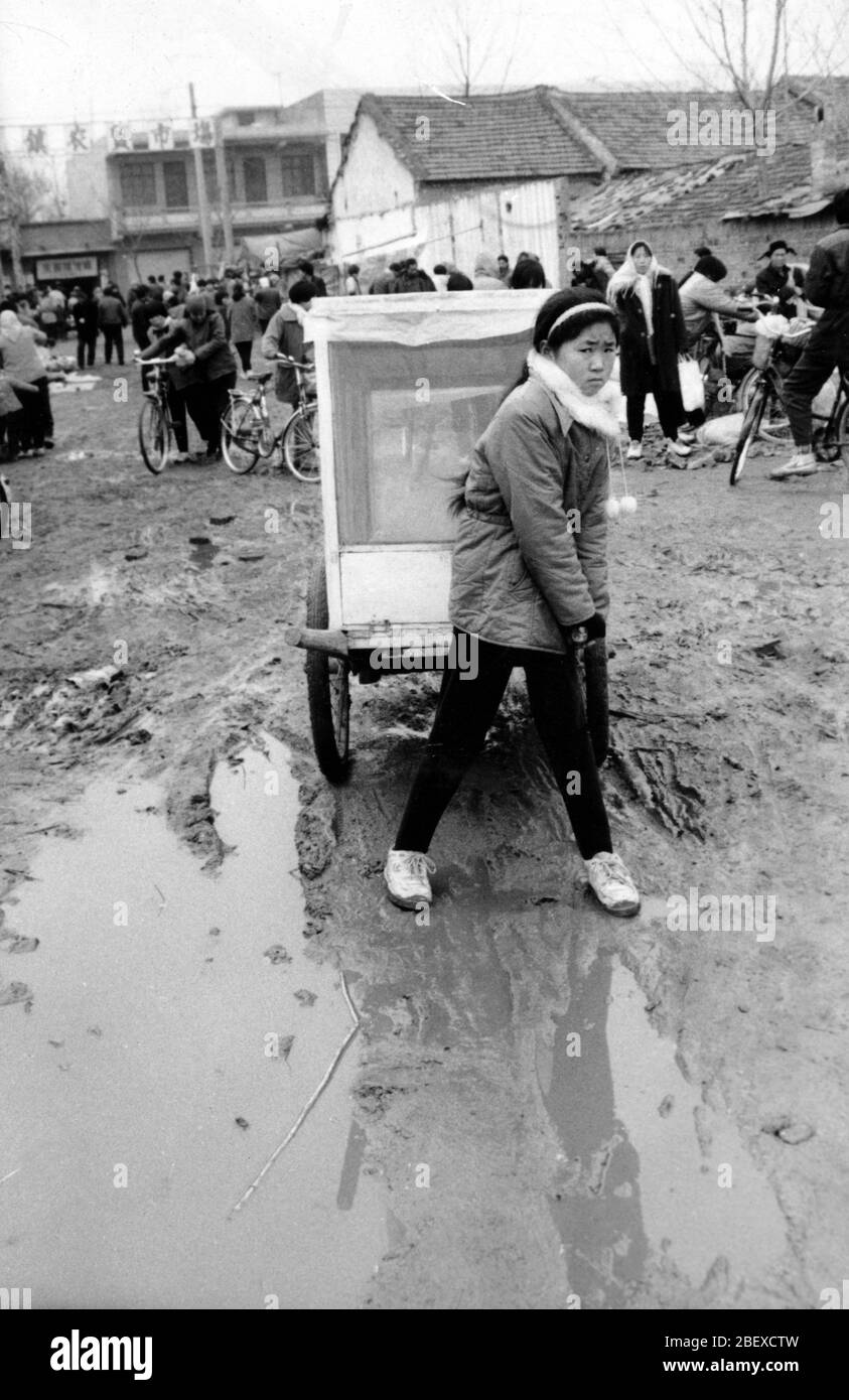 In den 1990er Jahren Zhangliang Town Lushan Henan schlammige Landstraße bei der Rallye wollte das kleine Mädchen ein Auto ziehen, aber es gab eine Pfütze auf dem schlammigen Ro Stockfoto